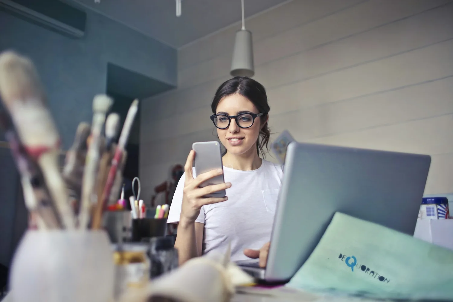 Uma empreendedora conferindo o celular na sua mesa, com o notebook aberto